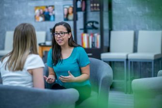 A woman in her early 30s explains something to a client who is sitting across from her. She looks passionate about what she is saying.