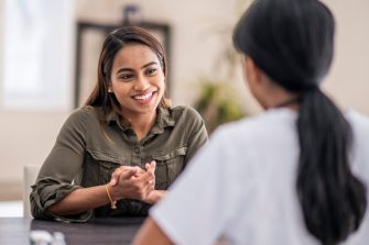 A stressed-out woman is chatting with her mental health counselor. She is explaining her problems. She is staying positive with a smile.