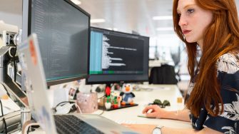 Female student sitting at dual screen computer desk working with cyber security programming