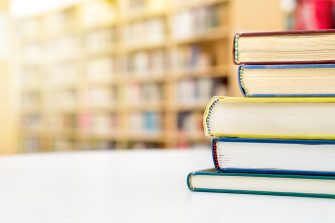 Stack and pile of books on table in public or school library.