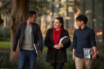 Three law students walking in front of Law Building, walking towards the camera, greenary and reflections in glass of Law Building in background