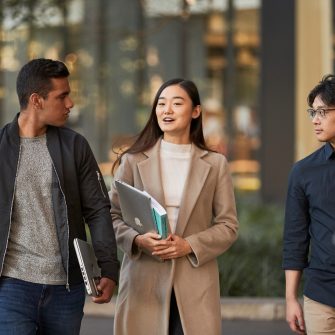 Three law students walking in front of Law Building, walking towards the camera, greenary and reflections in glass of Law Building in background