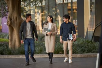 Three law students walking in front of Law Building, walking towards the camera, greenary and reflections in glass of Law Building in background