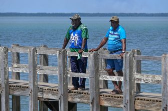 Two men on boardwalk looking out to ocean.