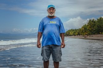 One of the community leaders in Kahingi stands where his gardens used to be over a decade ago before being slowly swept away into the sea. For years this community would see their beach-side homes slowly erode into the ocean without understanding what was happening until IOM staff