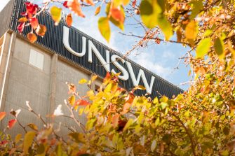 Looking close at the top of the Library tower building with white UNSW lettering. Top of autumn leaf trees in the foreground frame three sides.