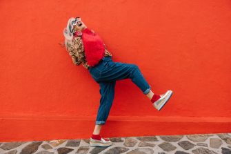 Excited senior woman dancing and having fun against a red background. Happy elderly woman feeling youthful and vibrant while wearing colourful clothing. Active mature woman celebrating her retirement.