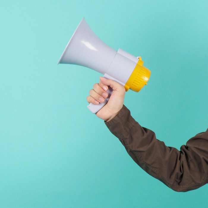 Hand is hold megaphone and wear navy color shirt on green or mint or Tiffany Blue background.