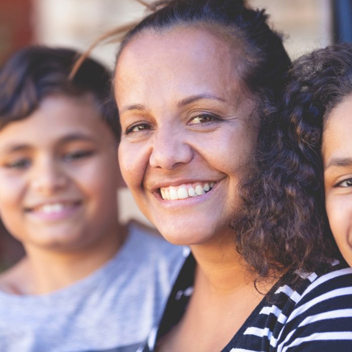 Aboriginal Family portrait with 1 parent and 2 children. They are sitting on the front porch. Everyone is happy and smiling. Could be a single mother.