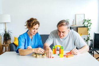 Professional nurse caregiver in geriatric clinic helps senior man with Alzheimer's disease - Old patient playing puzzle in retirement home - Healthcare and medical concept