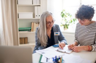 A senior woman volunteer helping Ukrainian woman to fill in forms at asylum centre.