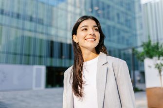 Portrait of young successful entrepreneur woman standing over modern company office building. Startup, vision and female empowerment