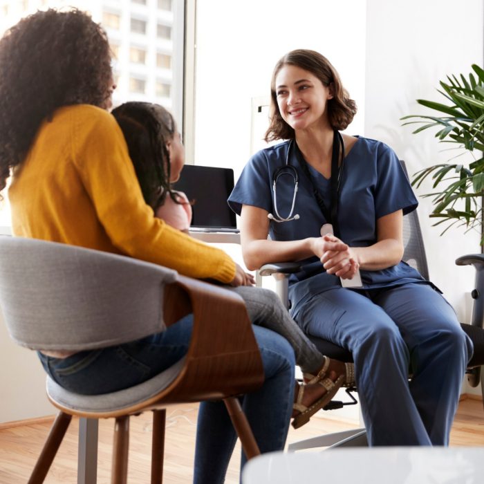 Mother And Daughter Having Consultation With Female Pediatrician Wearing Scrubs In Hospital Office
