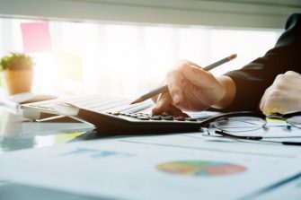 Close up Business woman using calculator and laptop for do math finance on wooden desk in office and business working background, tax, accounting, statistics and analytic research concept