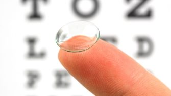 Contact lens on finger and snellen eye chart. The eye test chart is shown blurred in the background.