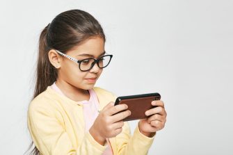 Smartphone use, cause eye damage for children. Child wearing eyeglasses looks at smartphone