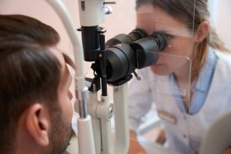 side view portrait of female ophthalmologist is looking through the slit lamp while examining eyesight of man patient in clinic
