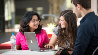 Two women and a man casually work at a laptop
