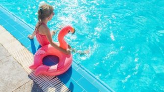 child sitting on edge of pool with flamingo blow up floaty
