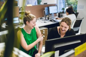 Two female UNSW colleagues laughing while working at their desks