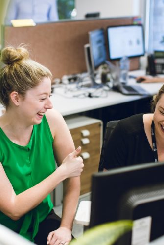 Two female UNSW colleagues laughing while working at their desks