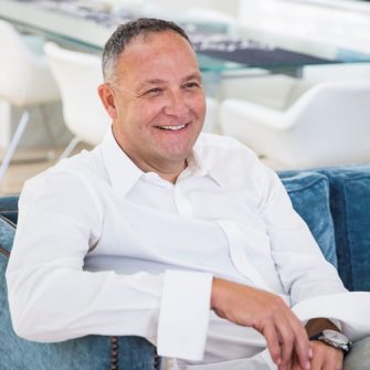 Headshot of Tony Surtees in a white shirt sitting on a blue sofa