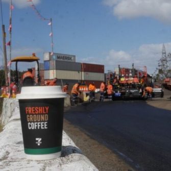 takeaway coffee cup in foreground with road crew laying asphalt in the background