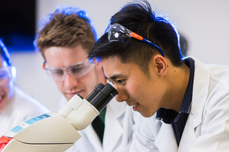 Three students one looking through a microscope