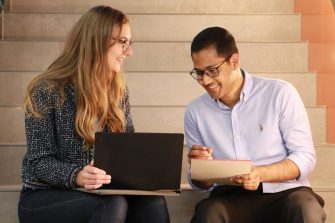 Two people sitting on stairs looking at laptop