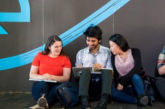 Students sitting beside a wall discussing work
