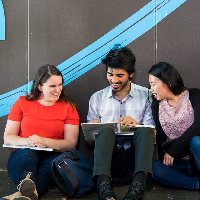 Students sitting beside a wall discussing work