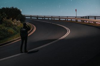 Man standing in the middle of the road looking at night sky