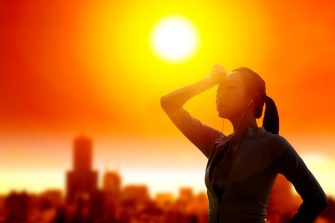 Woman shielding her eyes from sun with summer heat wave in the city background