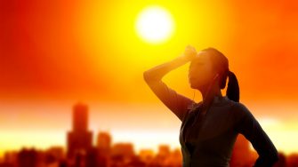 Woman shielding her eyes from sun with summer heat wave in the city background