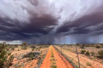 Storm moving in from horizon in desert along a fenceline