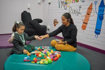 Woman sitting with child around circular mat with toys