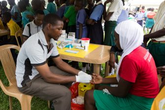 Nkokonjeru, Uganda. June 22 2017. A young man testing a girl for HIV by pricking her finger and drawing blood.