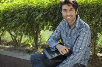 Smiling man sitting on plant bed holding a laptop