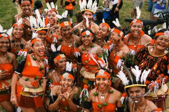 A woman in Indigenous dress stands in front of a see-through marquee shaped like a dome.