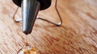 Close up of hot wax glue gun dripping glue onto a wooden table