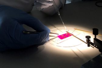 Gloved hand performing experiment on small square of pink material
