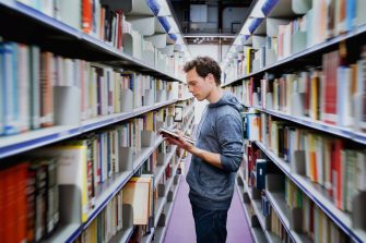 young student reading book between the shelves in the library