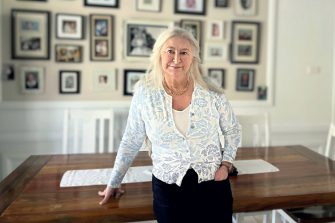 Theresa Flavin stands in her dining room, leaning on a table, in front of a wall of family photos. 