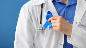 Doctor with blue ribbon on color background, closeup. Prostate cancer concept