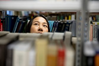 Student looking through library book shelves