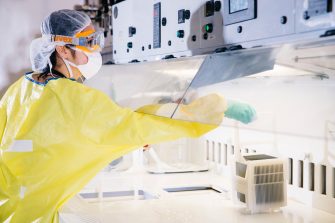 Student in lab with yellow lab coat, gloves, protective goggles and hairnet