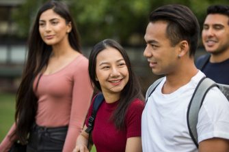 Students with backpacks walking across campus lawn