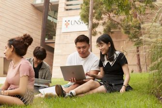 Students with backpacks and laptops sitting outside on campus