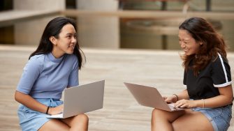 Students sitting and standing with laptops at outdoor courtyard