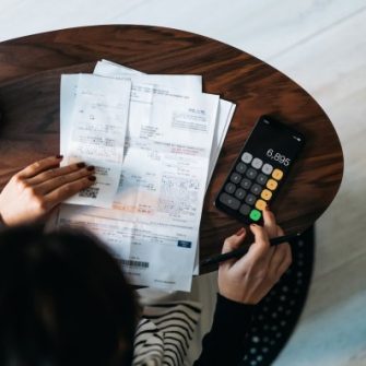 Overhead view of young Asian woman managing personal banking and finance at home. Planning budget and calculating expenses while checking her bills with calculator.